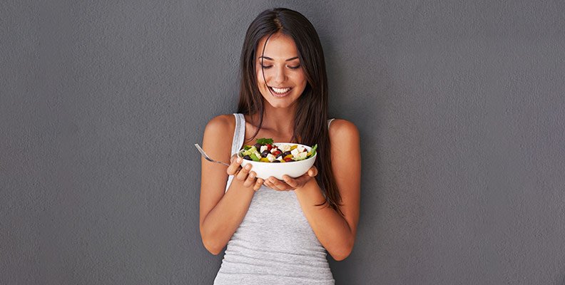 a woman holding up a bowl of salad